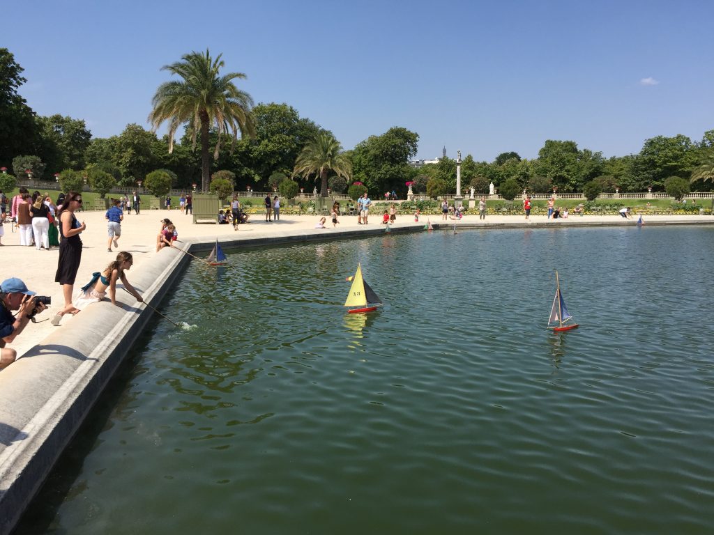 Kids poking sailboats with sticks on the pond in the gardens of Palais du Luxembourg