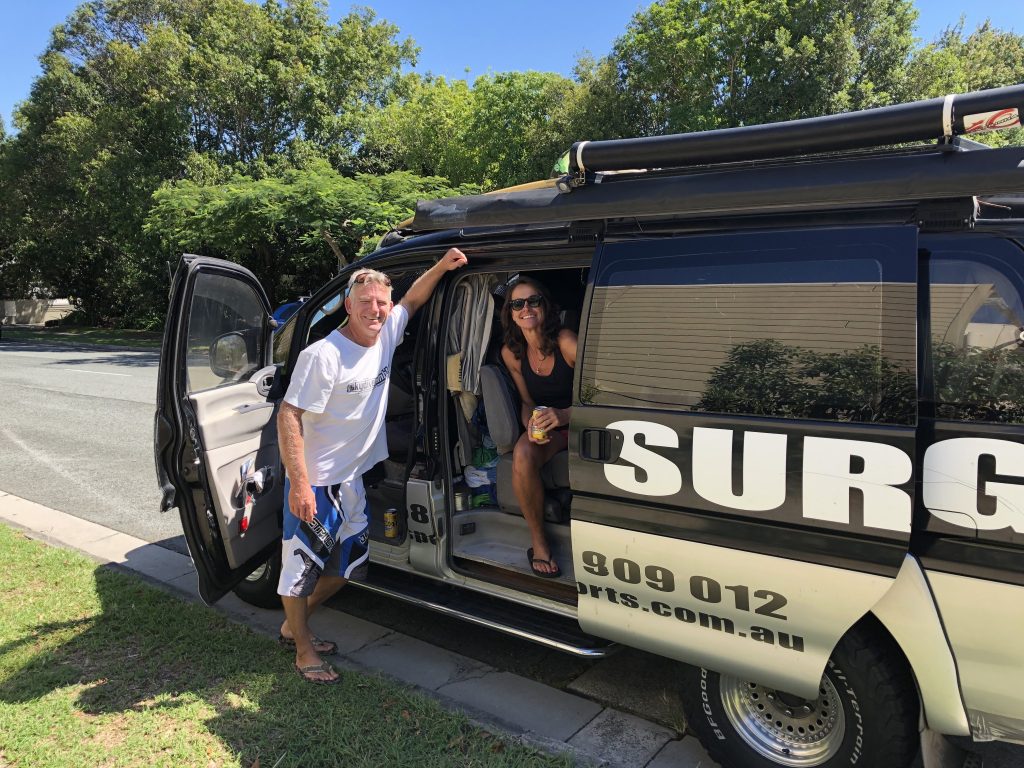 A woman sitting inside the van behind the driver's seat, with a man standing beside the van