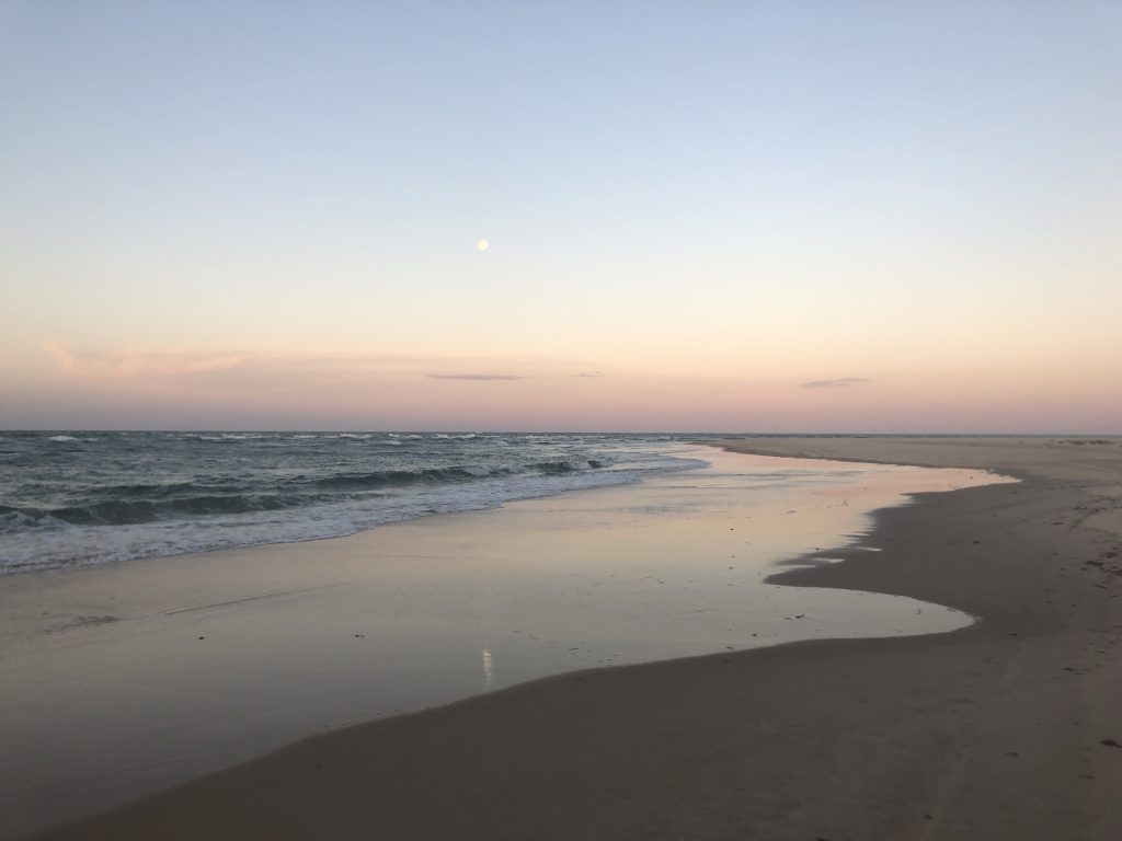 Moon ascending as the sun sets over the beach